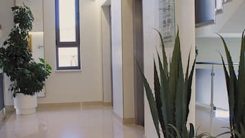 A hotel corridor with a reception desk, a large potted plant, and a staircase.