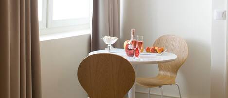 A dining area with a round table, two chairs, a bottle of Mateus wine, two glasses, and a bowl of whipped cream.