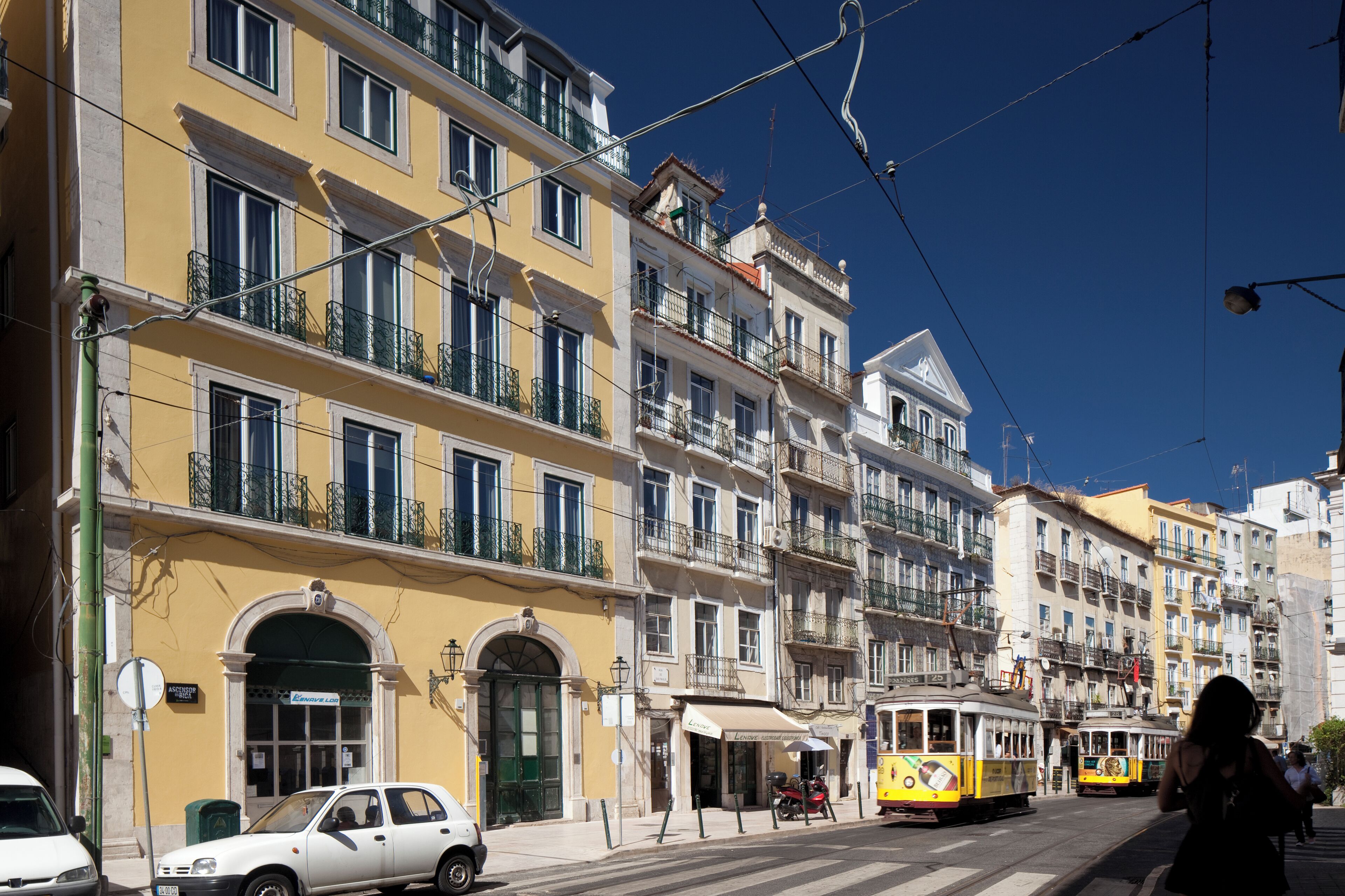 Ruas com edifícios amarelos, um eléctrico e um carro branco.