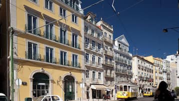Ruas com edifícios amarelos, um eléctrico e um carro branco.