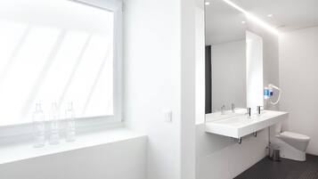 Uma casa de banho moderna com uma janela grande, três garrafas de água, uma pia branca e uma sanita.