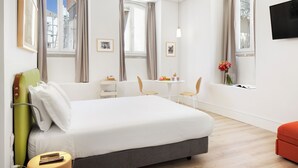 A hotel room with a bed, a desk, two chairs, a small table, a TV, and a window with curtains. - LSA Ascensor da Bica by Numa (Lisbon)