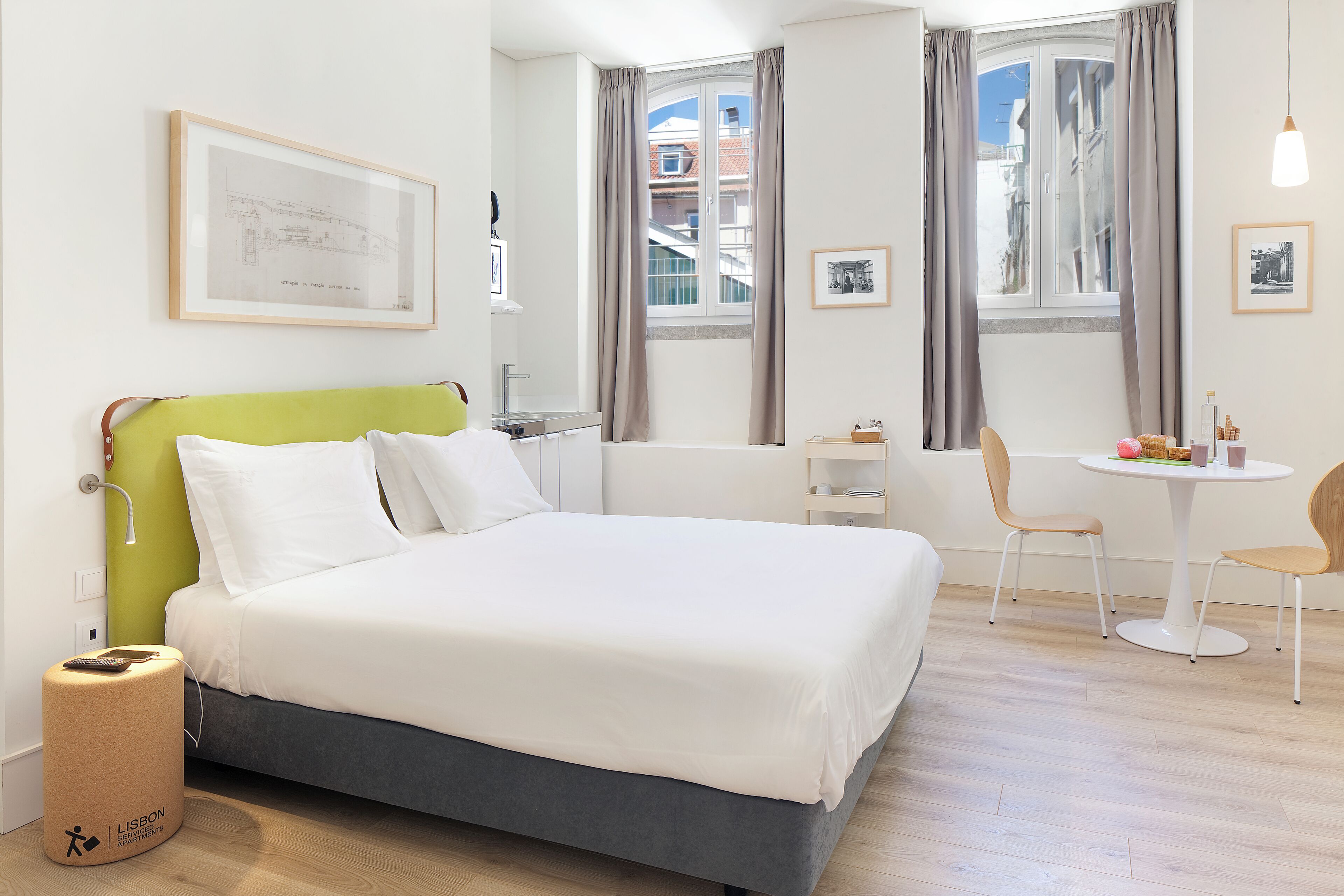 Ein Hotelzimmer mit einem Bett, einem kleinen Tisch mit Stühlen, einem Fenster mit Vorhängen und einem gerahmten Bild an der Wand.