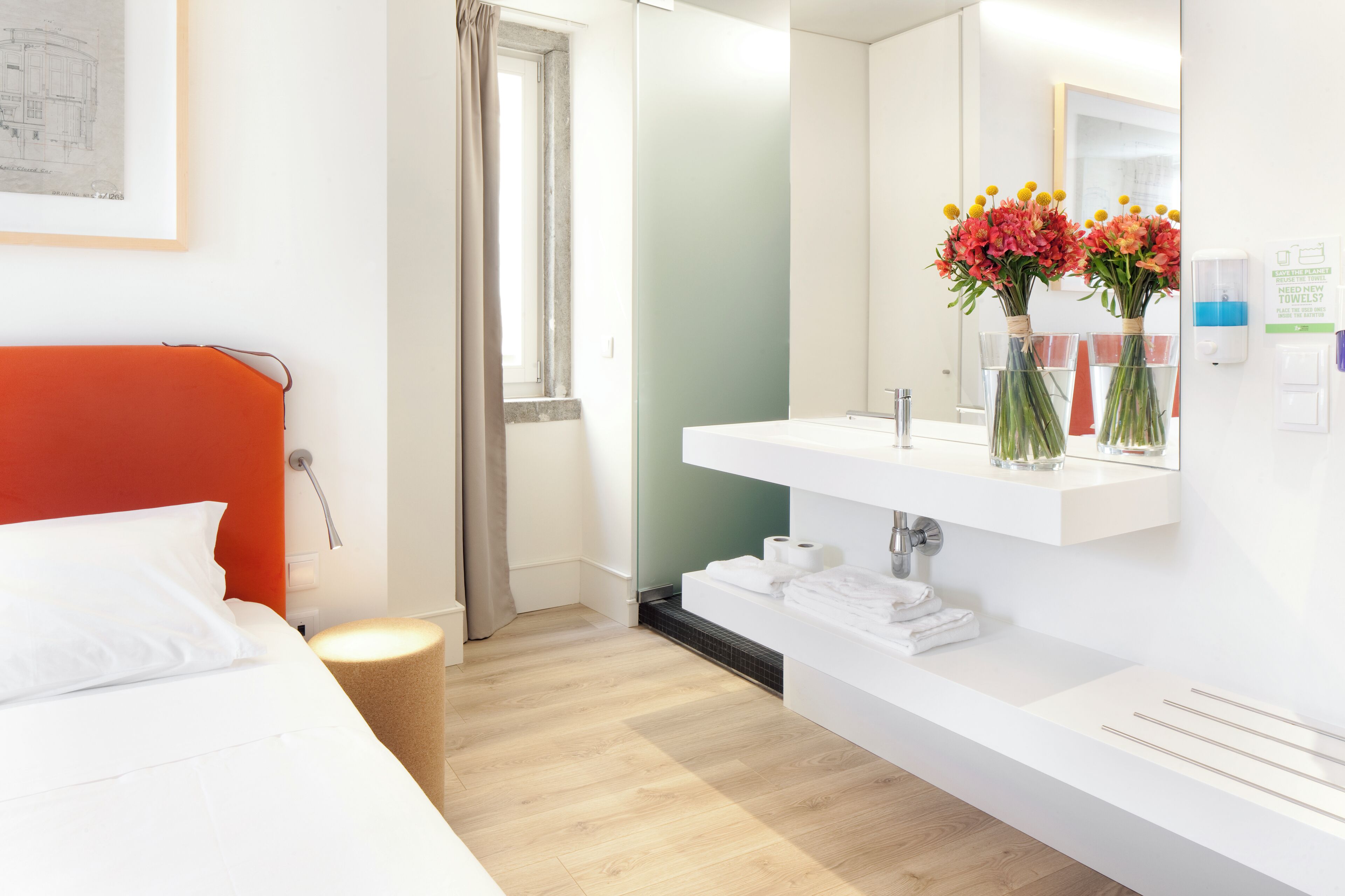 Una camera d'albergo moderna con un letto, un bagno con un lavandino bianco e una finestra con tende.