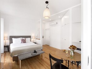 Ein modernes Hotelzimmer mit einem Bett, Nachttischlampen, einer Bank, einem Esstisch mit Stühlen und einer Pendelleuchte.