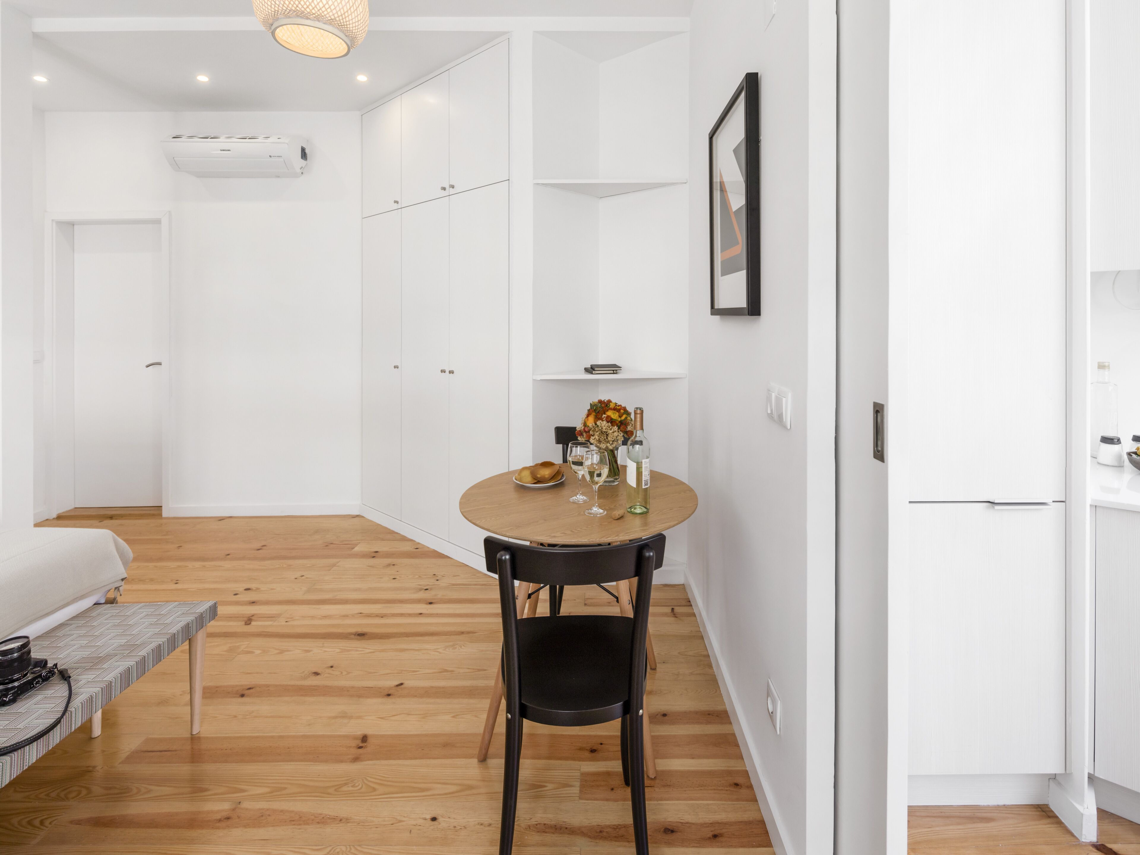 Une pièce moderne et minimaliste avec un plancher en bois, une table de salle à manger ronde accompagnée d’une chaise, un canapé et une petite table basse.