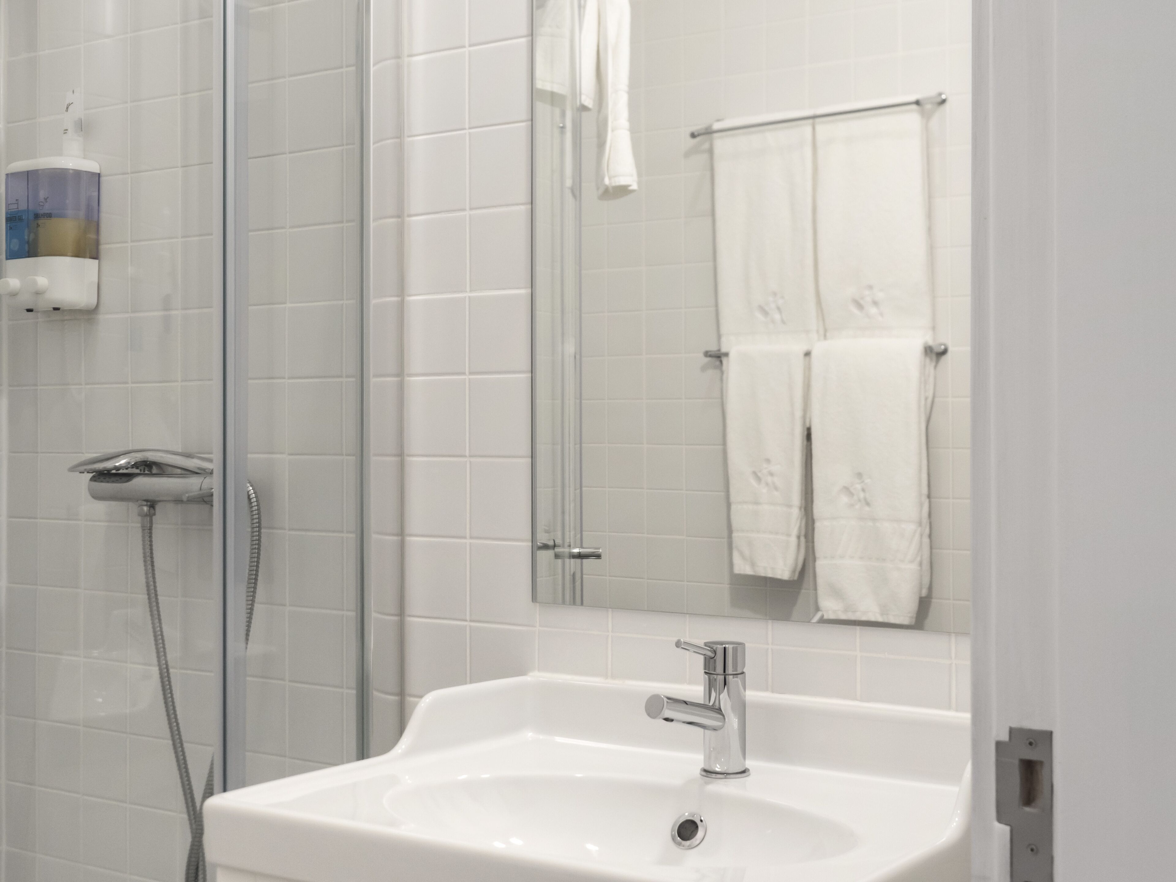Ein Badezimmer mit einem weißen Waschbecken, einem Spiegel und einer Duschkabine.