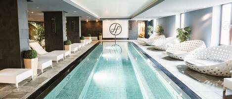 Una piscina con sillones de descanso y un logotipo en la pared.