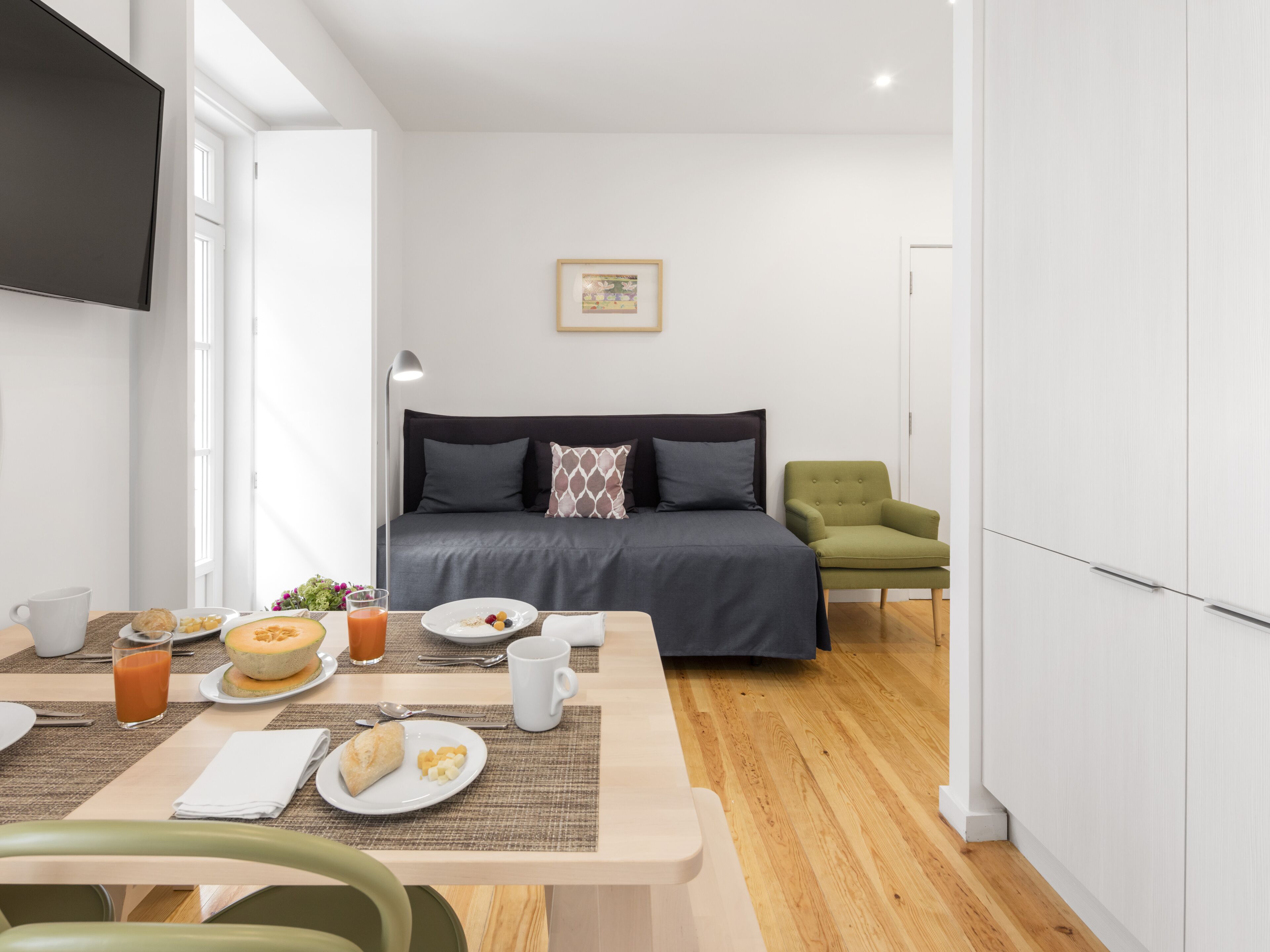 A modern room with a bed, a dining table with breakfast, and a green armchair.