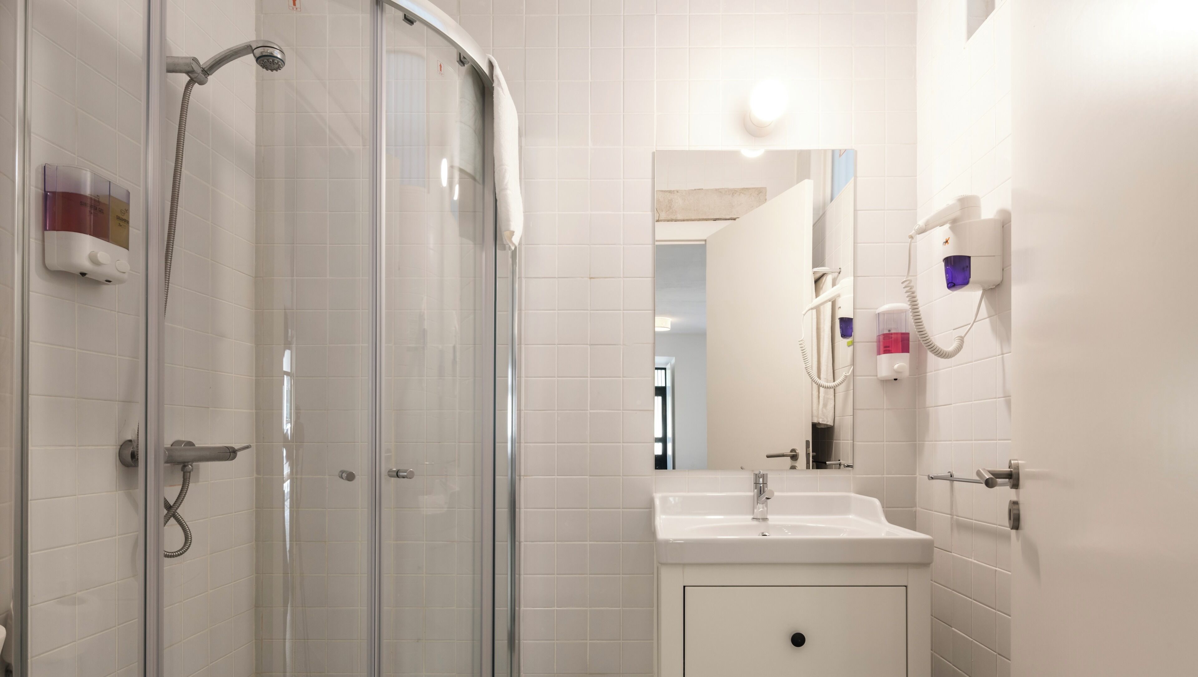 A bathroom with a glass-enclosed shower, a sink, a mirror, and a towel rack.