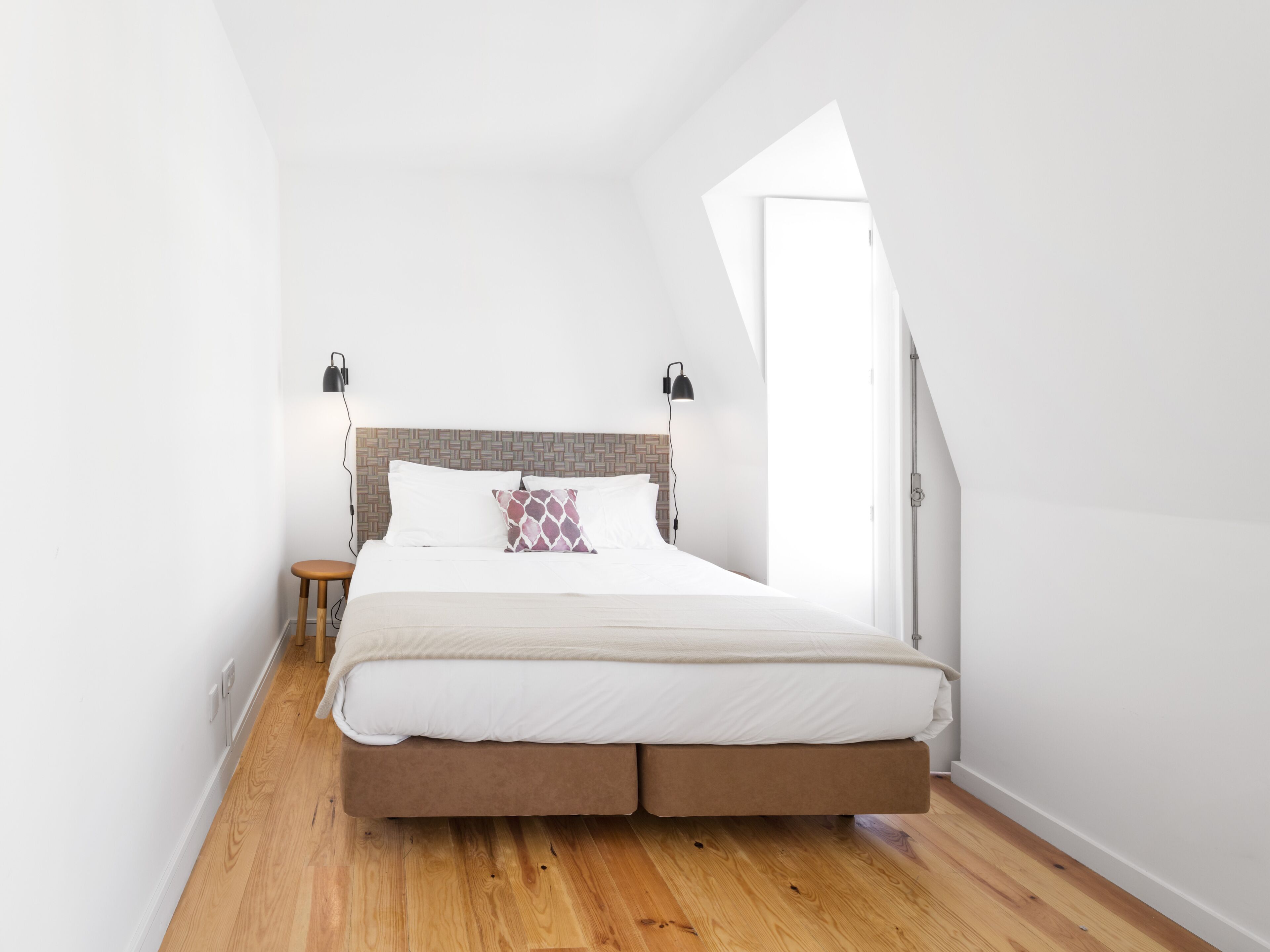 Ein Schlafzimmer mit Bett, Nachttischlampen, einem Nachttisch und einer schrägen Decke.