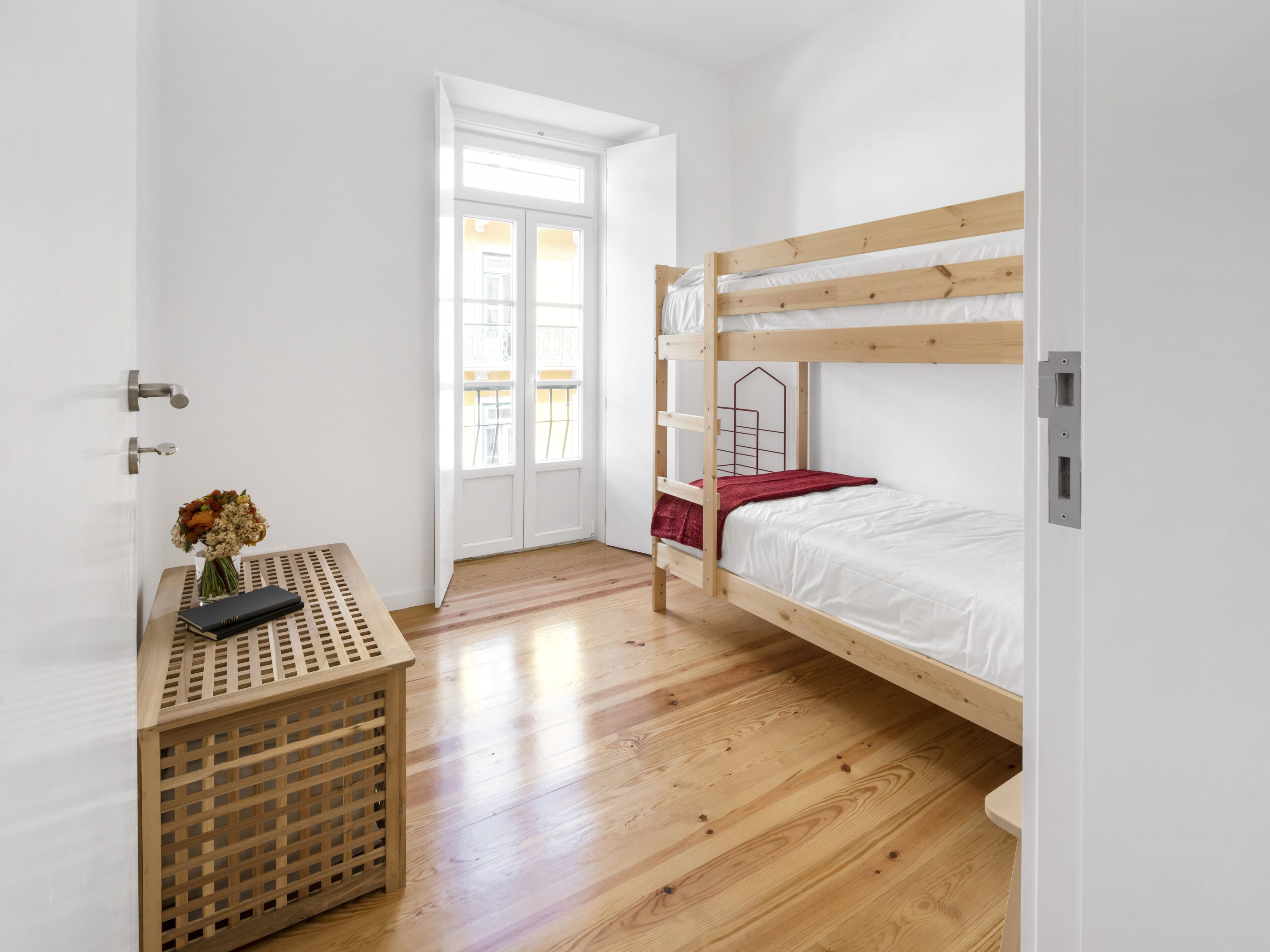 Une chambre avec un lit superposé, un plancher en bois, un bureau agrémenté d’un vase de fleurs et une porte donnant sur un balcon.