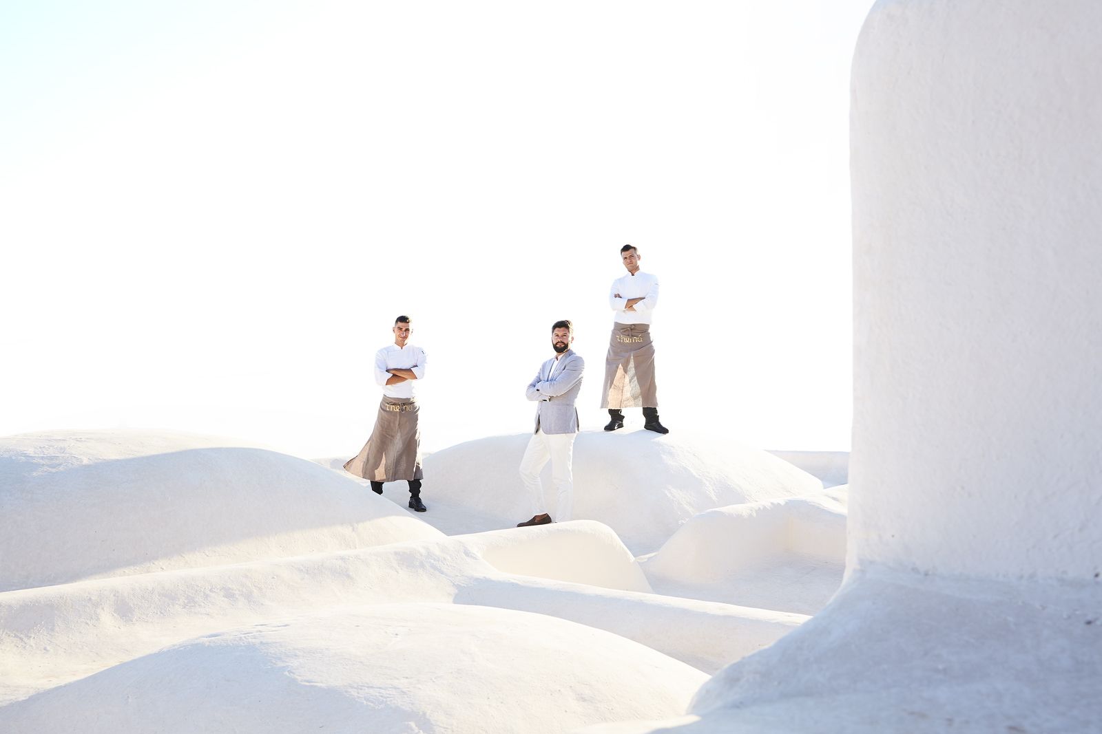 Three individuals standing on a white sandy surface with a clear sky in the background.