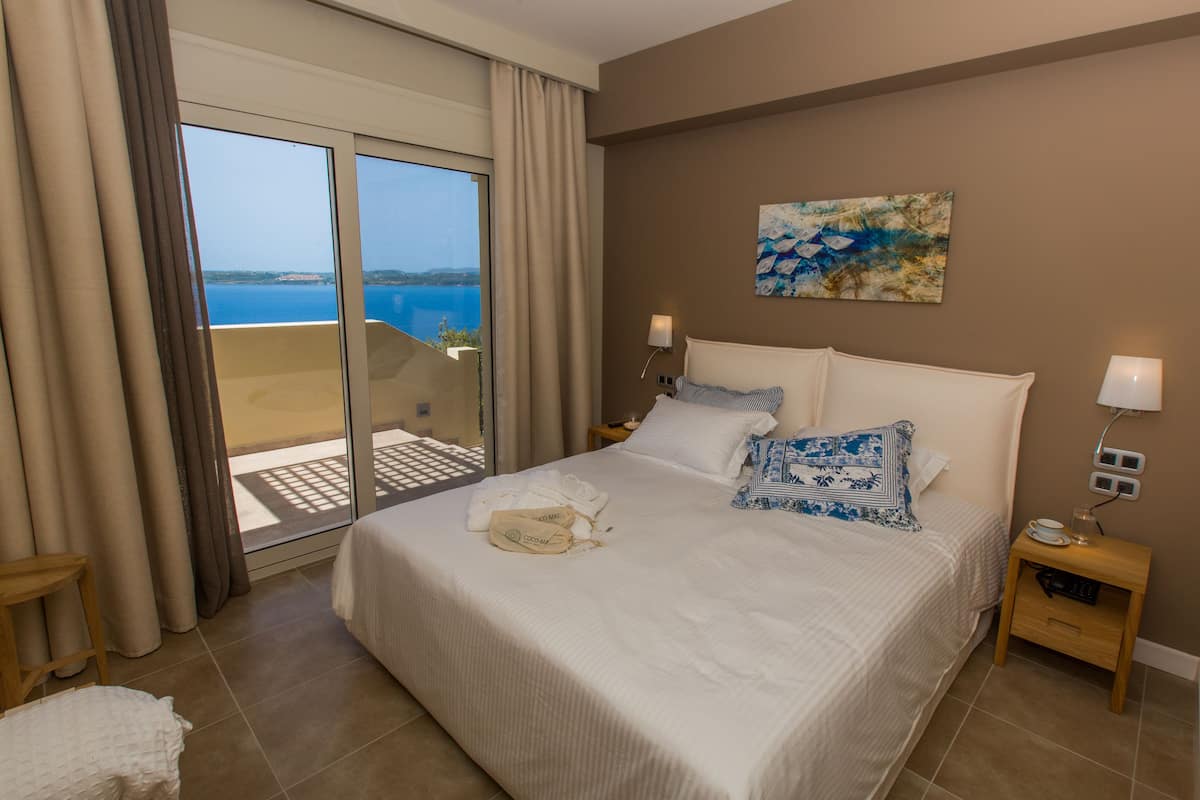 A hotel room with a bed, a nightstand, a painting, and a view of the sea.