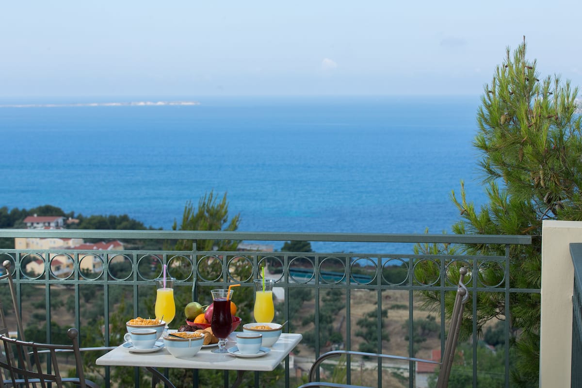 A balcony with a table set for breakfast overlooking a coastal view.