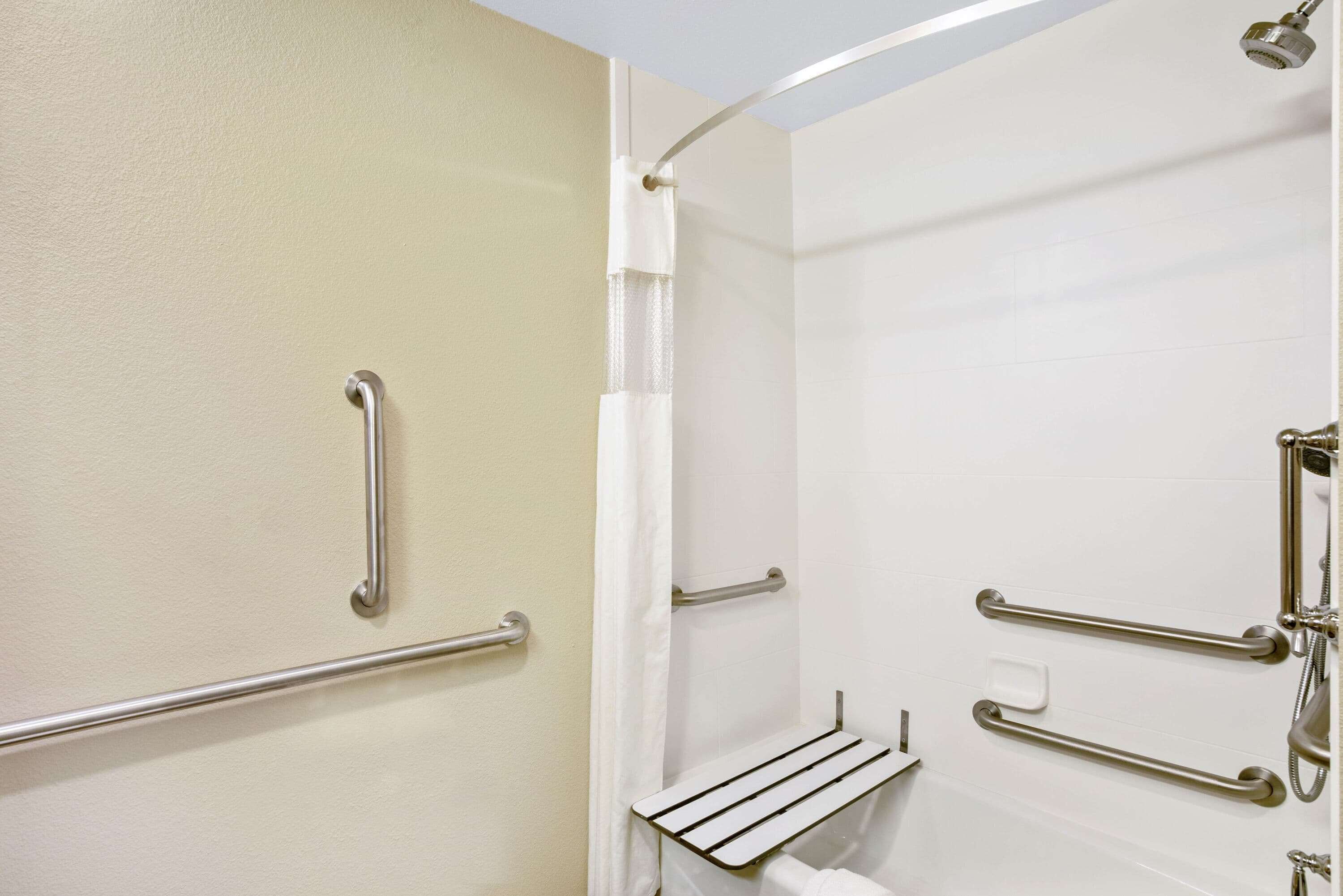 Un baño con ducha, barras de apoyo, un perchero y un jabonera.