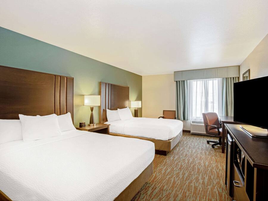 A hotel room with two beds, a desk with a television, and a chair.