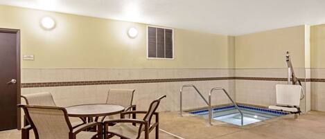 A hotel room with a pool, a table with chairs, and a door.
