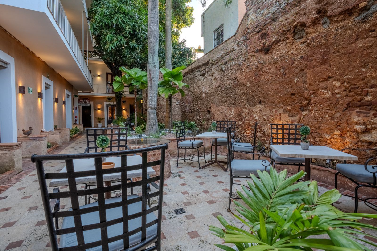 An outdoor patio with tables and chairs, surrounded by stone walls and greenery.