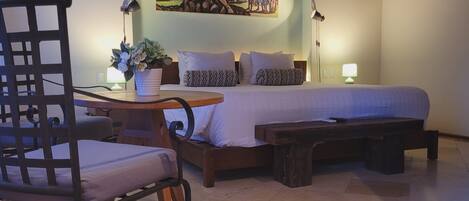 A bedroom with a bed, a chair, a nightstand, a lamp, and a painting on the wall.