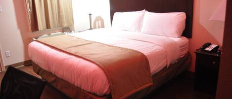 Una habitación de hotel con cama, mesita de noche, una silla y una ventana con cortinas.