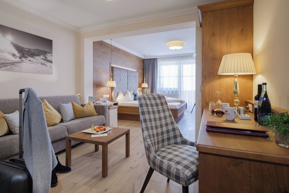 Une chambre d’hôtel moderne, équipée d’un canapé, d’un fauteuil, d’une table basse en bois et d’un bureau avec une lampe et une bouteille de vin.