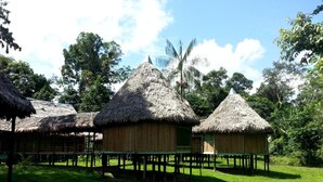 Thatched-roof huts with wooden stilts, surrounded by lush greenery and a calm water body. - Cumaceba Amazon Lodge (Belén)
