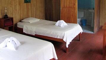A hotel room with two beds, a wooden floor, a wooden chair, and a small table with a lamp.