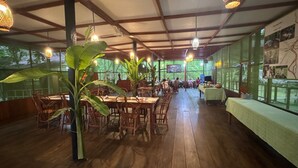 A restaurant with wooden tables and chairs, large windows, and hanging lights. - Cumaceba Amazon Lodge (Belén)