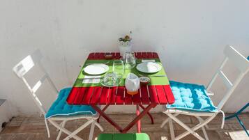 Una mesa de comedor con platos, vasos y una jarra, rodeada de sillas blancas con cojines azules.