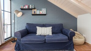 Una habitación con un sofá azul, un cojín a rayas, una lámpara y una estantería con cuadros enmarcados.