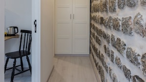 Un pasillo con pared de piedra, una puerta blanca y una pequeña mesa con una silla.