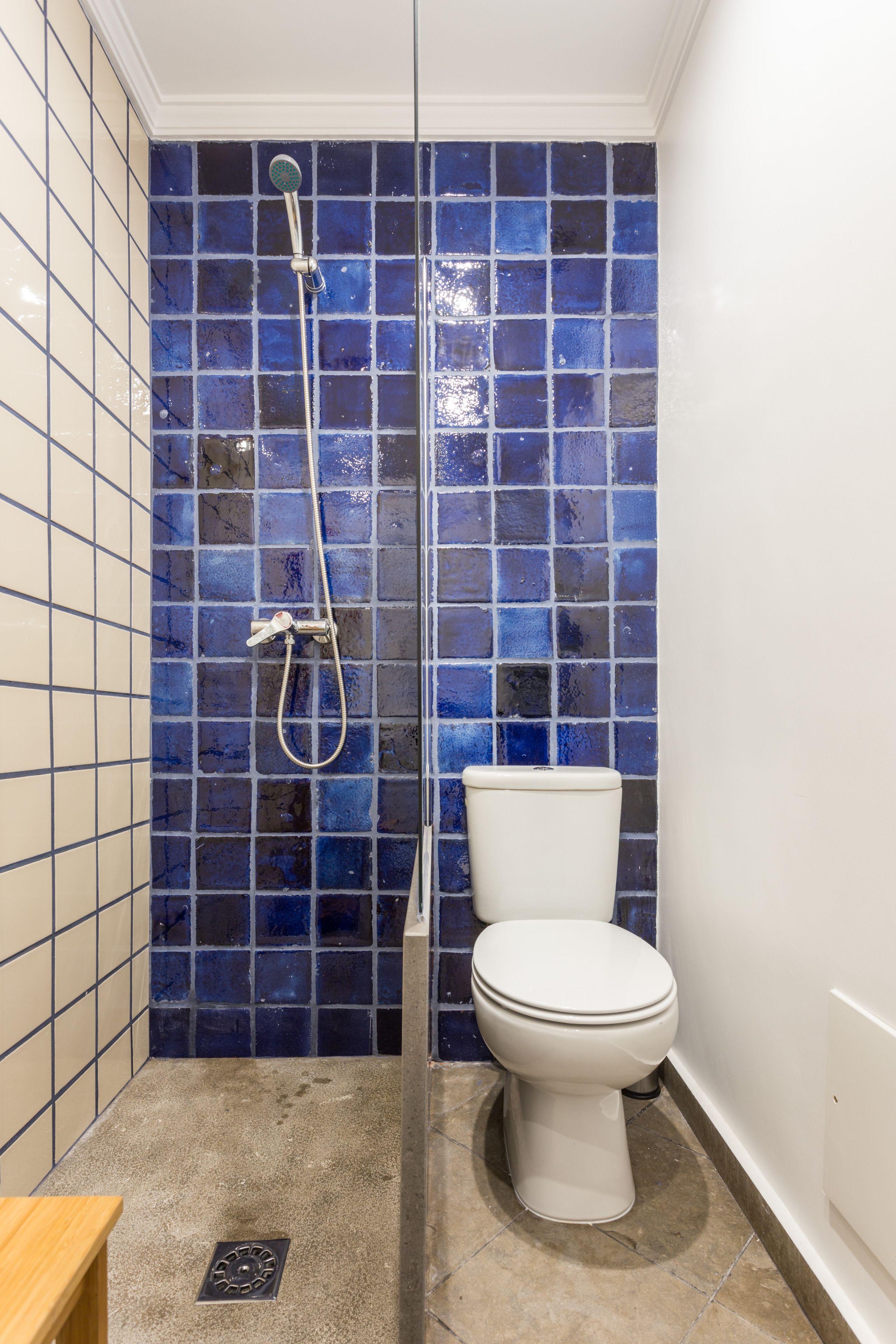 A bathroom with a white toilet, a shower with a blue mosaic tile wall, and a wooden bench.