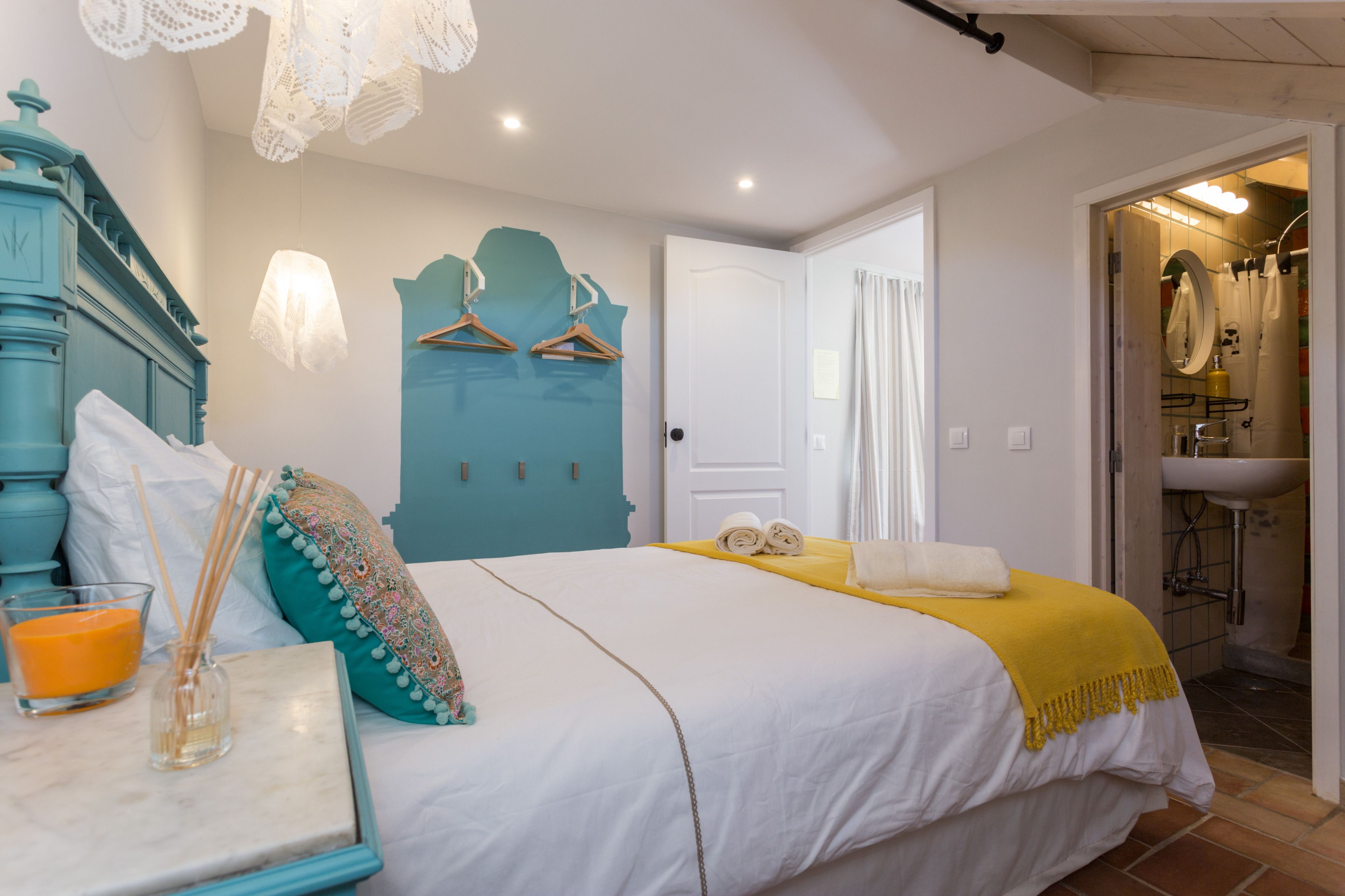 Une chambre à coucher avec un lit, une table de chevet sur laquelle se trouve une bougie, et une salle de bain visible à travers une porte ouverte.