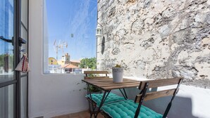 Un balcón con mesa y sillas, una planta en maceta y vistas de edificios y una iglesia.