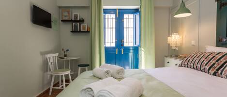 A hotel room with a bed, a chair, a small table, a TV, and a blue door.
