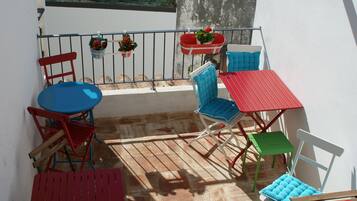 Un balcon avec une table rouge, des chaises bleues et rouges, et des plantes en pot.
