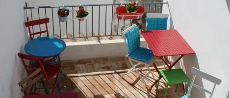 A balcony with a red table, blue and red chairs, and potted plants.