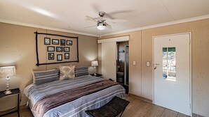 Un dormitorio con cama, mesitas de noche, ventilador de techo, cuadros en la pared y una puerta que da al baño.