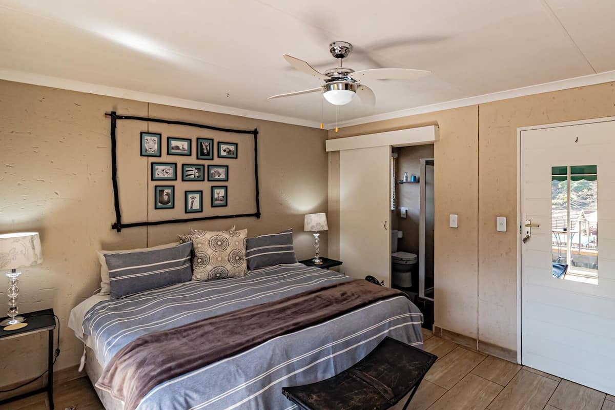 A bedroom with a bed, bedside tables, a ceiling fan, framed pictures on the wall, and a door leading to a bathroom.
