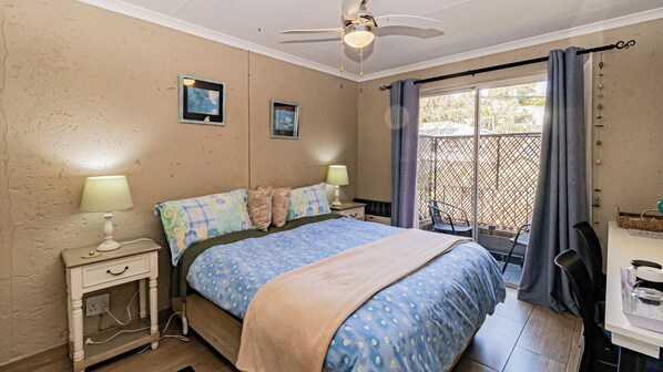 A bedroom with a bed, two bedside tables with lamps, a ceiling fan, a window with curtains, and a view of the outside. - BnB on 8th Avenue (Johannesburg)