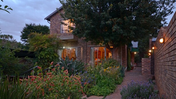 Una casa de ladrillo con un sendero en el jardín que lleva a la entrada, rodeada de plantas y flores diversas.