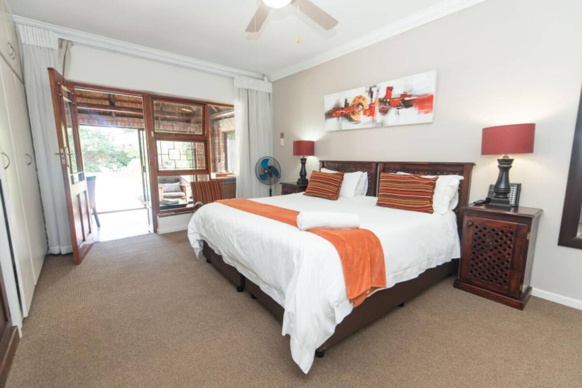 A spacious bedroom with a large bed, a ceiling fan, and a view through a sliding door to an outdoor area.