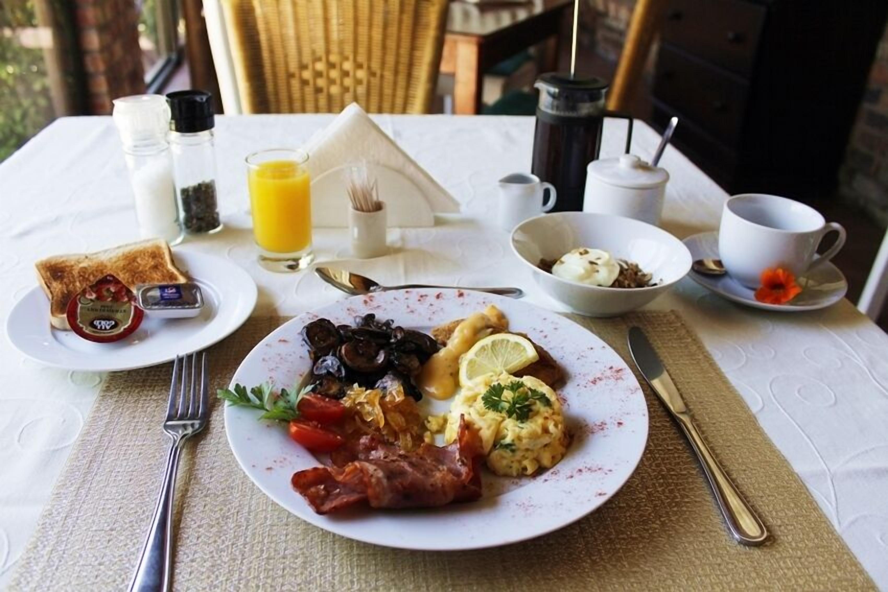 A breakfast setting with toast, scrambled eggs, bacon, mushrooms, and a glass of orange juice on a table.
