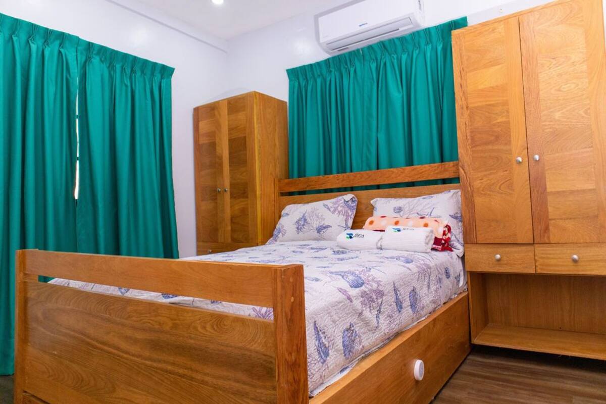 Un lit en bois avec une couvre-lit à motifs floraux, des rideaux turquoise et une armoire en bois.