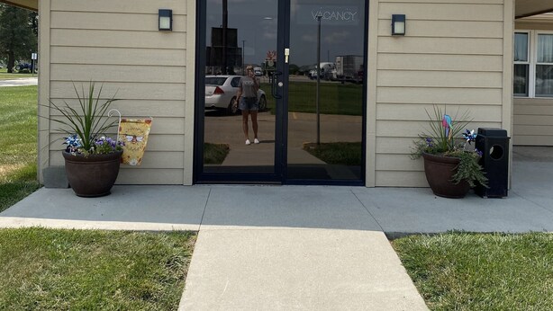 A small, single-story building with a flat roof and a large glass door. There are two potted plants on either side of the entrance, and a small trash can to the right. - Stuart Motor Lodge (Stuart)
