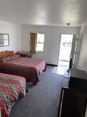 A hotel room with two beds, a desk, a television, and a door leading outside.