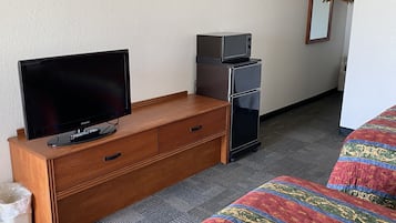 A hotel room with a wooden dresser, a television, a microwave, a small refrigerator, a bed with a colorful quilt, and a mirror on the wall.