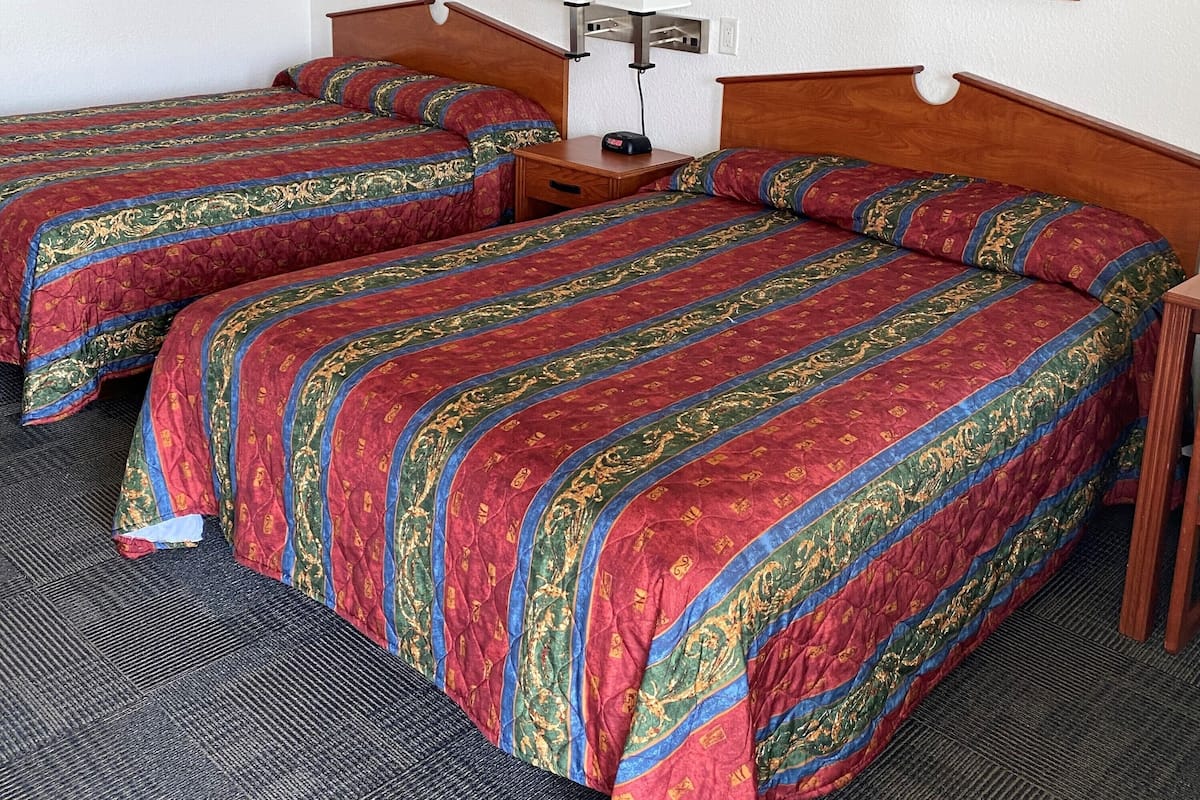 A hotel room with two beds, a nightstand, a lamp, and two framed pictures on the wall.