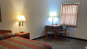 A hotel room with a bed, a desk, a chair, and a window with curtains. - Stuart Motor Lodge (Stuart)
